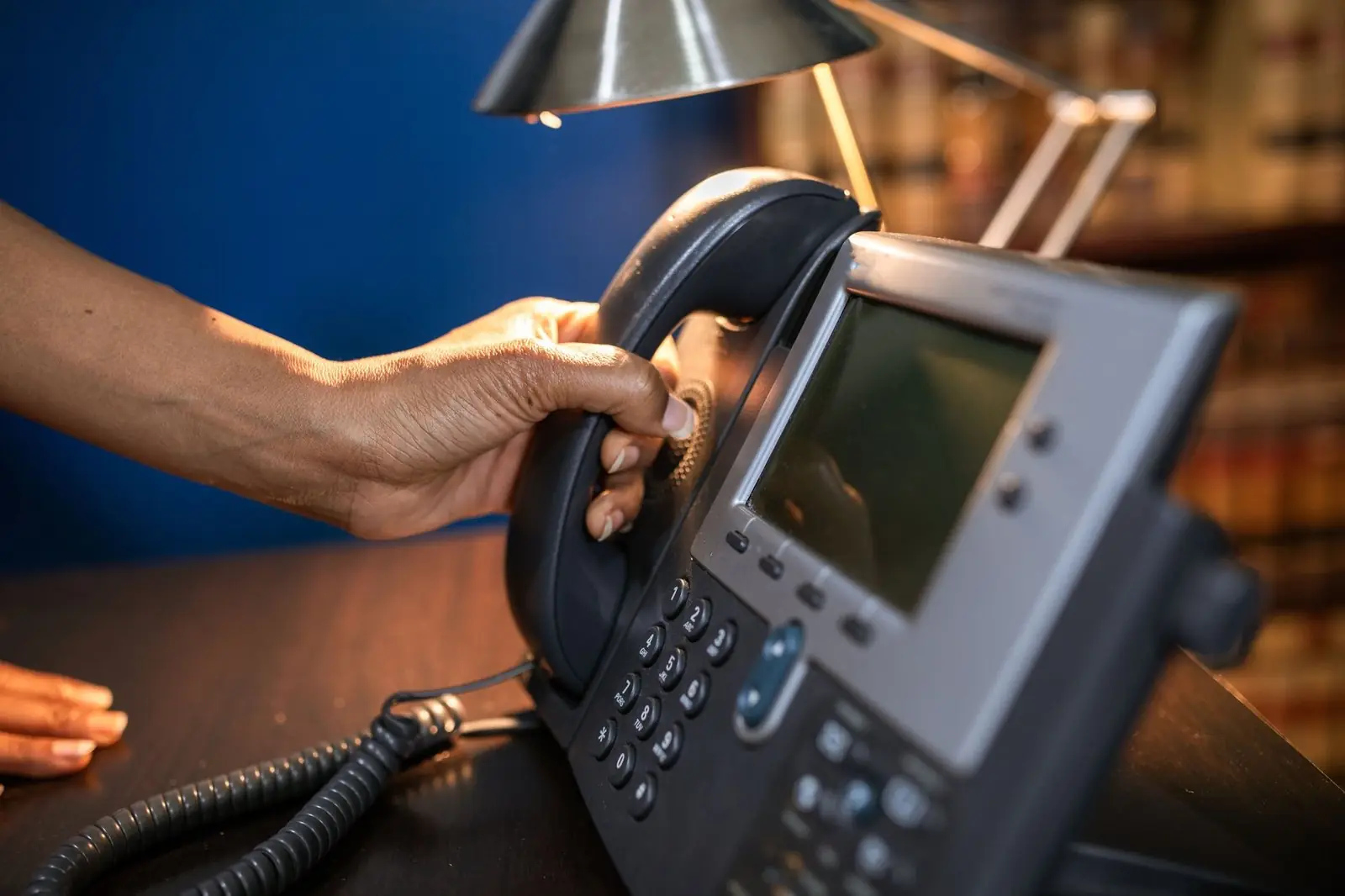 A hand dialling a desk phone on an office desk