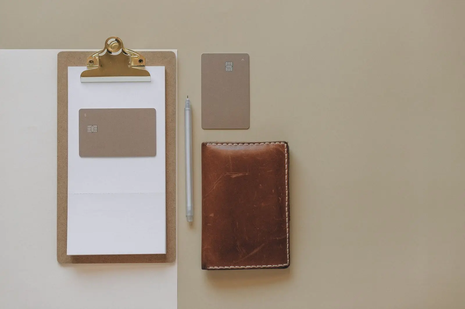 Clipboard, card, pen and leather wallet laid out on a desk