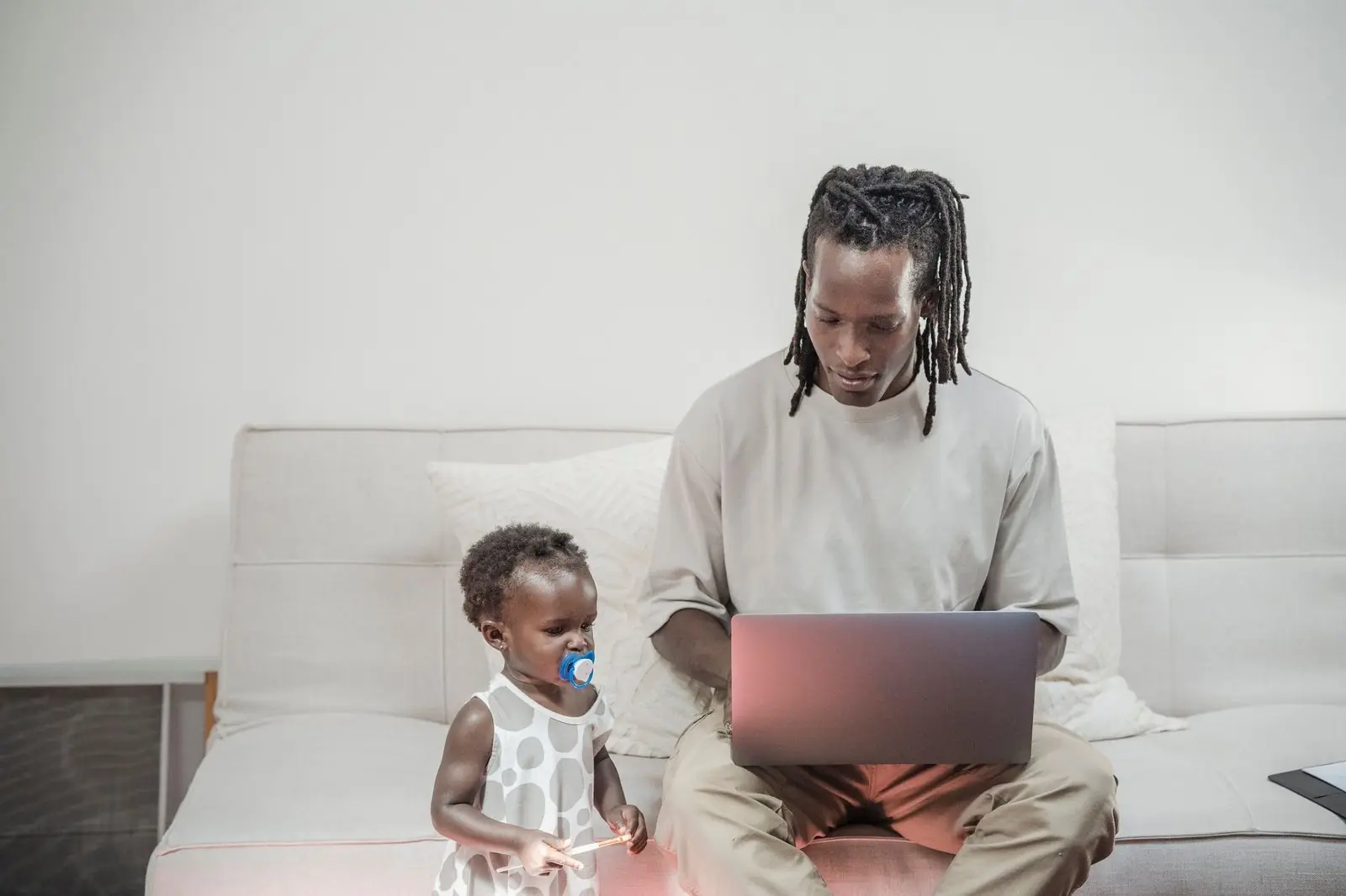 Father on a laptop at home with his toddler beside him