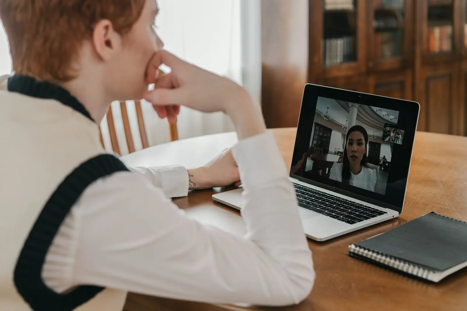 A woman on a video call at a laptop, taking notes