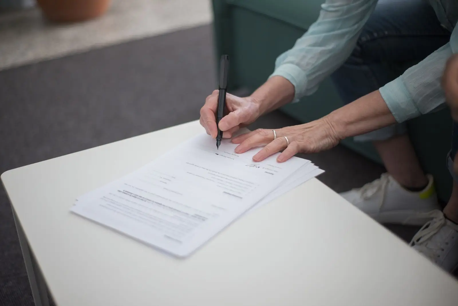Woman signing a stack of printed pages on a low table