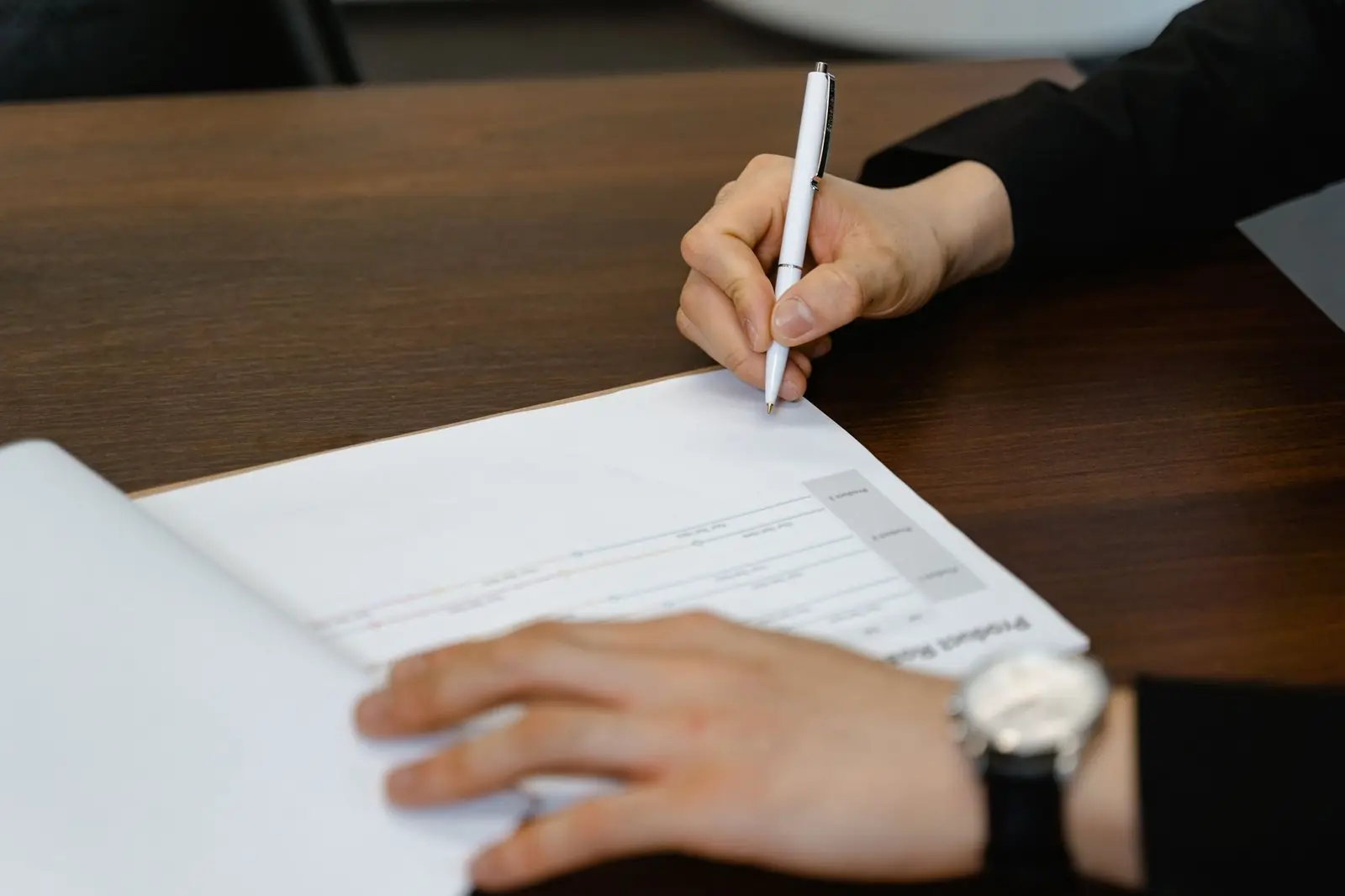 Person signing a printed document at a wooden desk