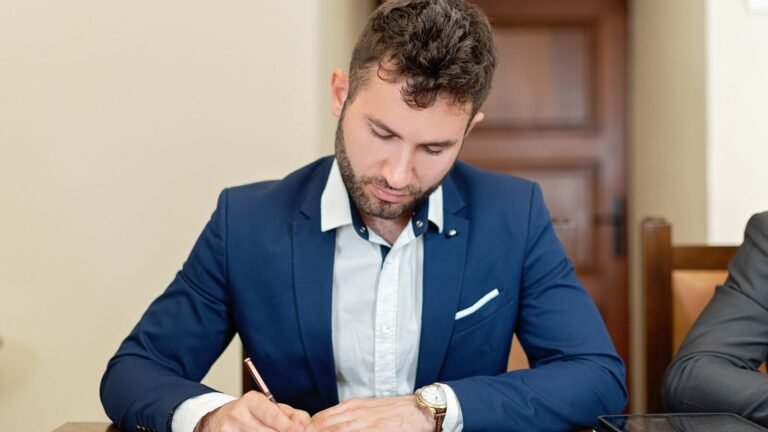 Man in a blue suit signing a power of attorney document at an office desk