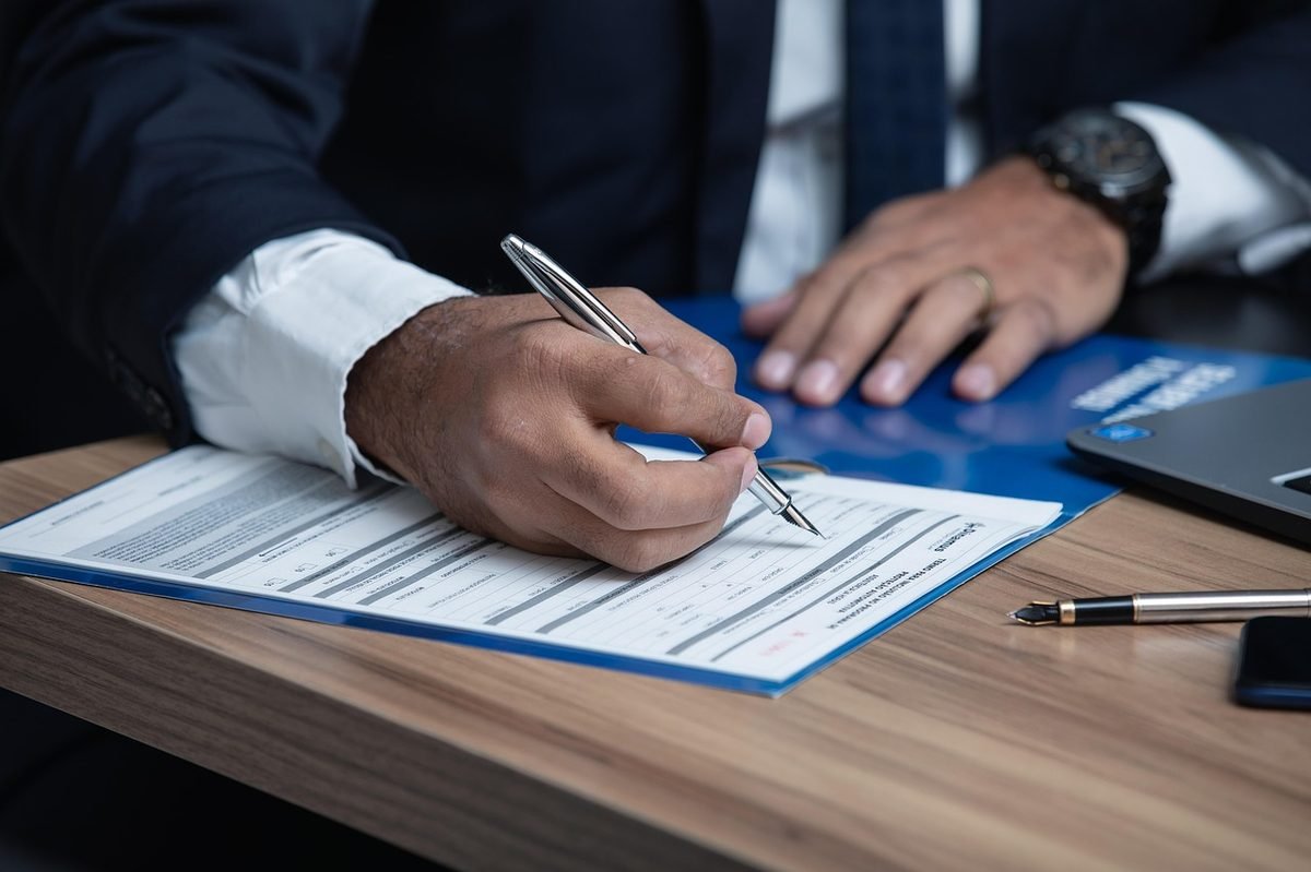 Hand holding a silver pen over a form on a wooden desk