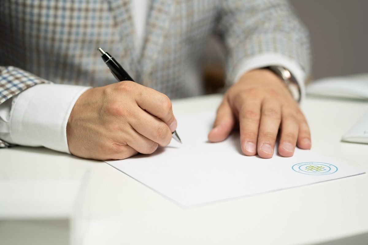 Hand signing a Dubai Land Department power of attorney with a pen on a white desk