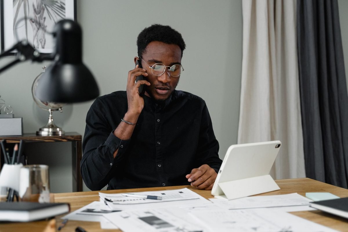 Man at a desk with papers and a tablet taking a work phone call