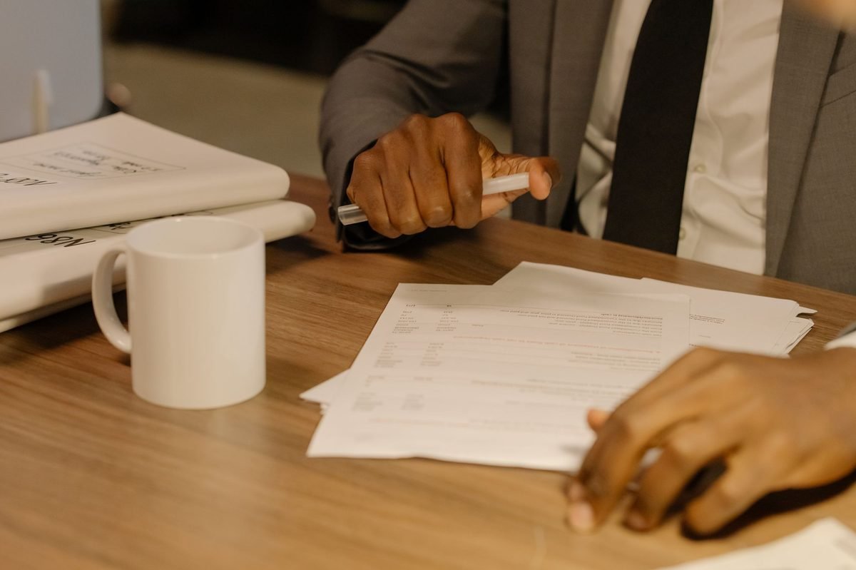 Man in a suit going through loose papers on a wooden desk with a mug